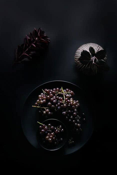Fotografía cenital de un tazón de uvas y otros accesorios sobre un fondo oscuro