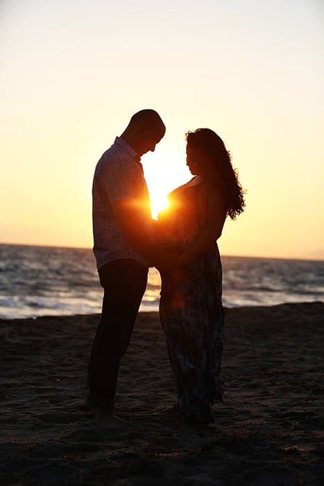 foto de una pareja en una playa con el sol poniéndose de fondo