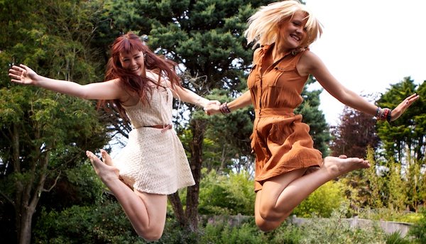 Foto de dos mujeres jóvenes saltando mientras se toman de la mano