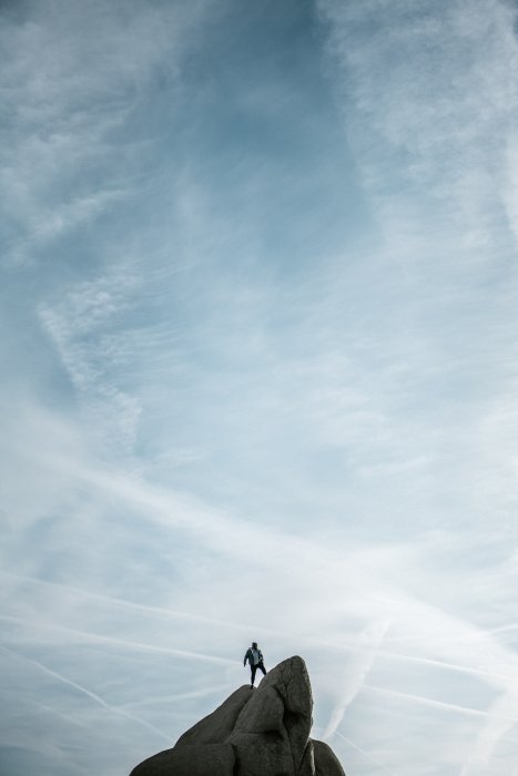 Una persona de pie sobre una roca, con un cielo azul detrás de ellos 