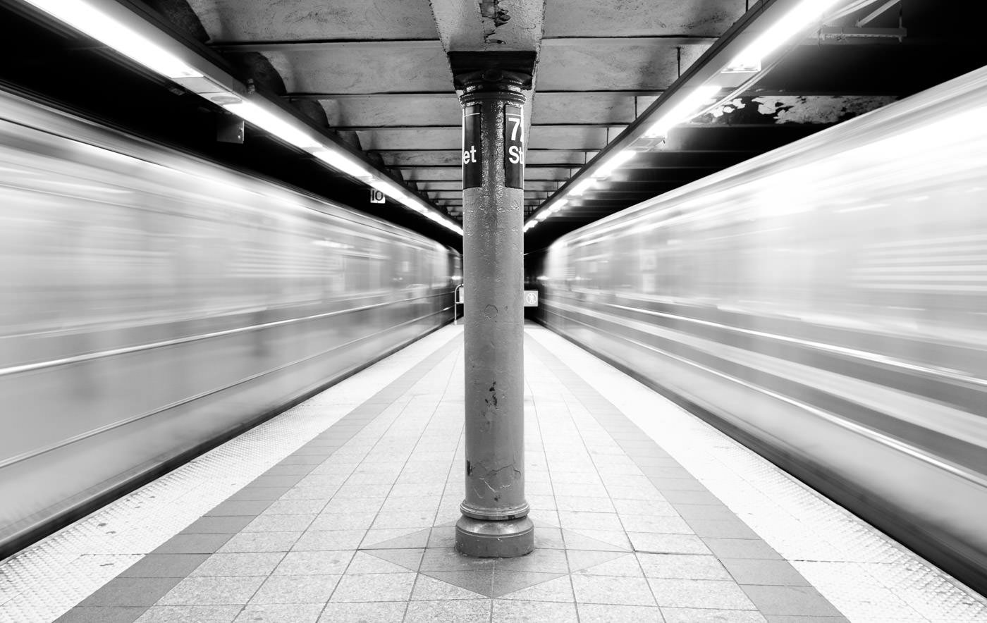 Trenes del metro de NYC corriendo a ambos lados de la plataforma, creando un espacio borroso alrededor del centro