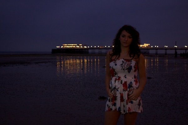 Fotografía de retrato de una niña de pie en una playa.  Fotografía crepuscular.