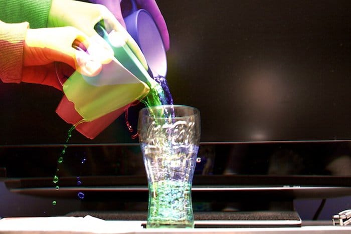 Efecto Harris de manos coloridas que vierten agua colorida en un vaso
