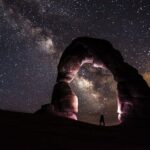 Una impresionante fotografía nocturna con un hombre bajo un arco de piedra y un cielo estrellado