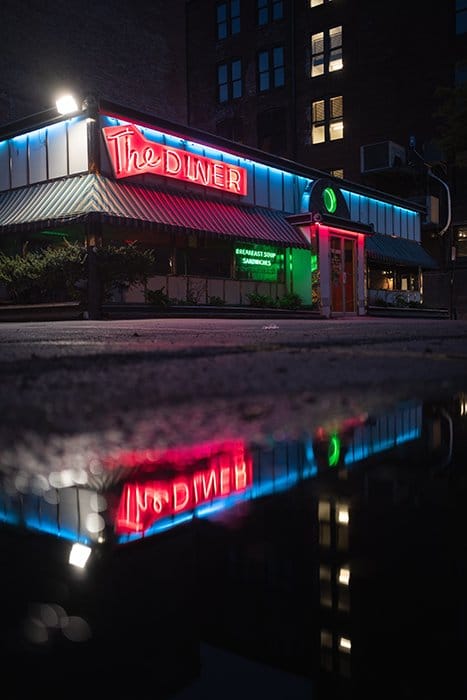 Los letreros de neón rojo de un restaurante reflejados en un charco debajo - fotografía con luz de neón