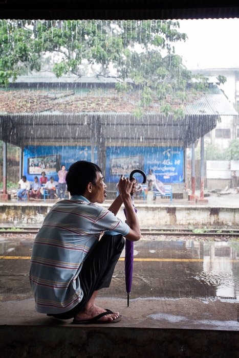 Fotografía de viaje de un hombre con paraguas refugiándose de la lluvia tropical. 