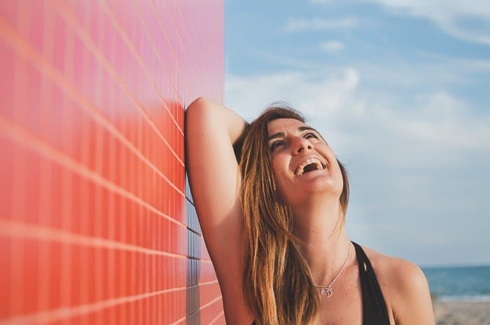 Una mujer riendo bajo el sol junto a una pared roja.